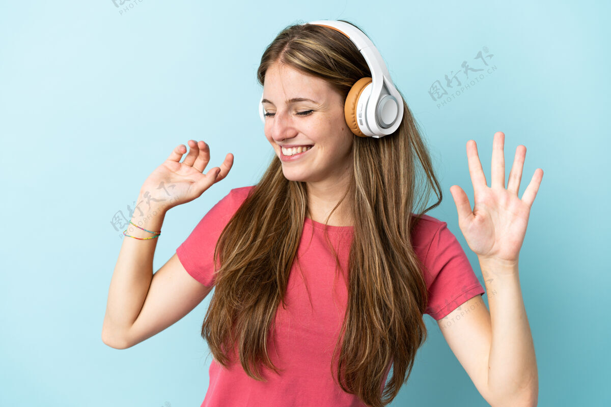年轻年轻的白种女人在蓝色的背景下听音乐和跳舞女孩休闲表演