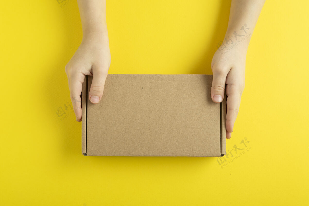 棕色纸板箱在儿童手上黄色背景 顶视图交货纸板纸张