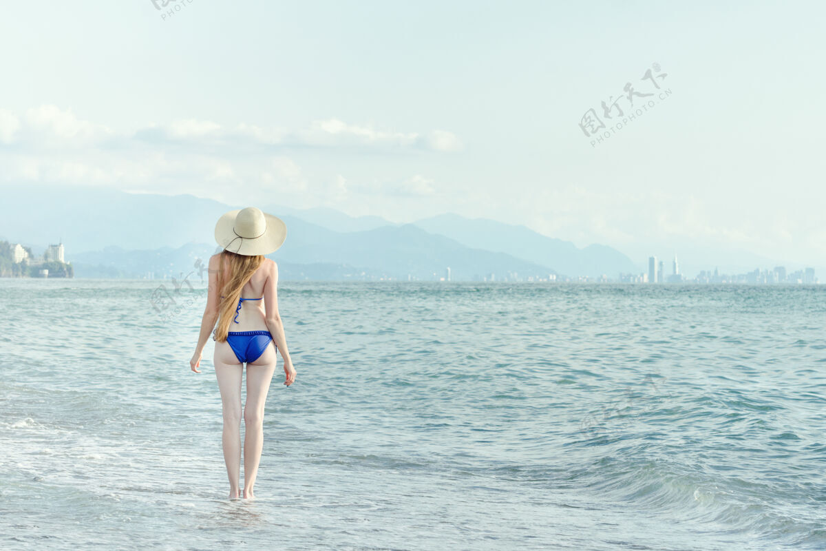晒黑穿泳衣戴帽子的女人走过海景从后面格鲁吉亚女孩蓝色
