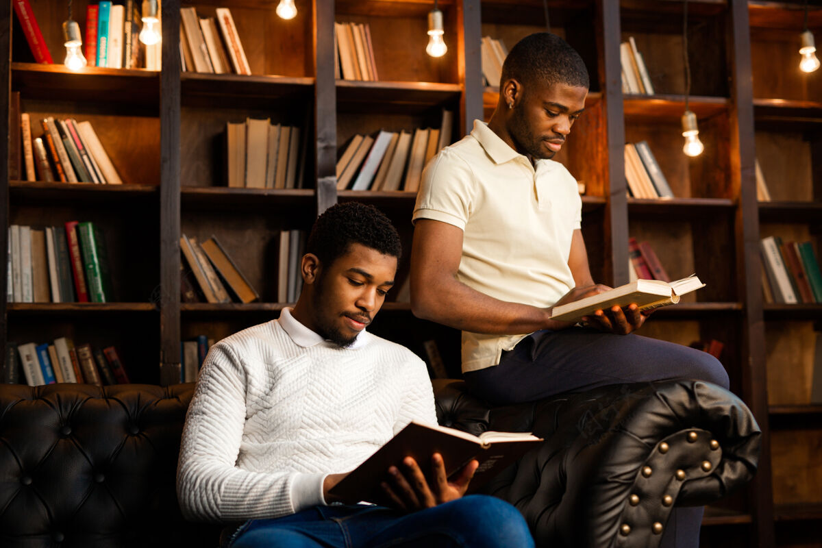 民族两个年轻的非洲男人正坐在沙发上看书大学人学生