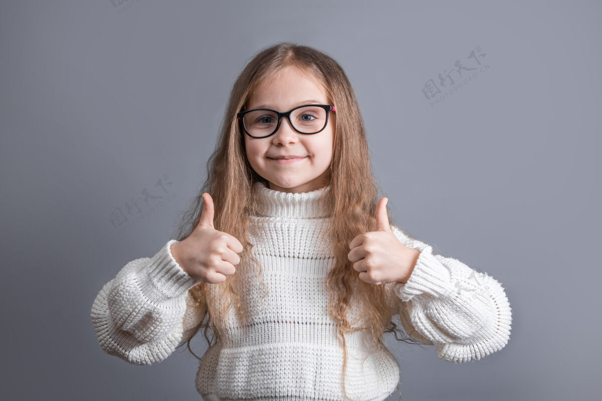 情绪一个年轻迷人的小女孩的肖像 金发飘逸 穿着白色毛衣 微笑着竖起大拇指 像是在唱歌文本.复制空间快乐积极快乐