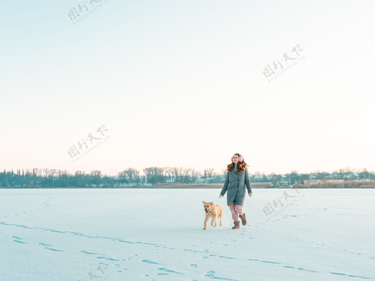 金毛猎犬冬季公园里的一位年轻女子和她的金毛狗散步寻回犬友谊宠物和人类拉布拉多公园年轻
