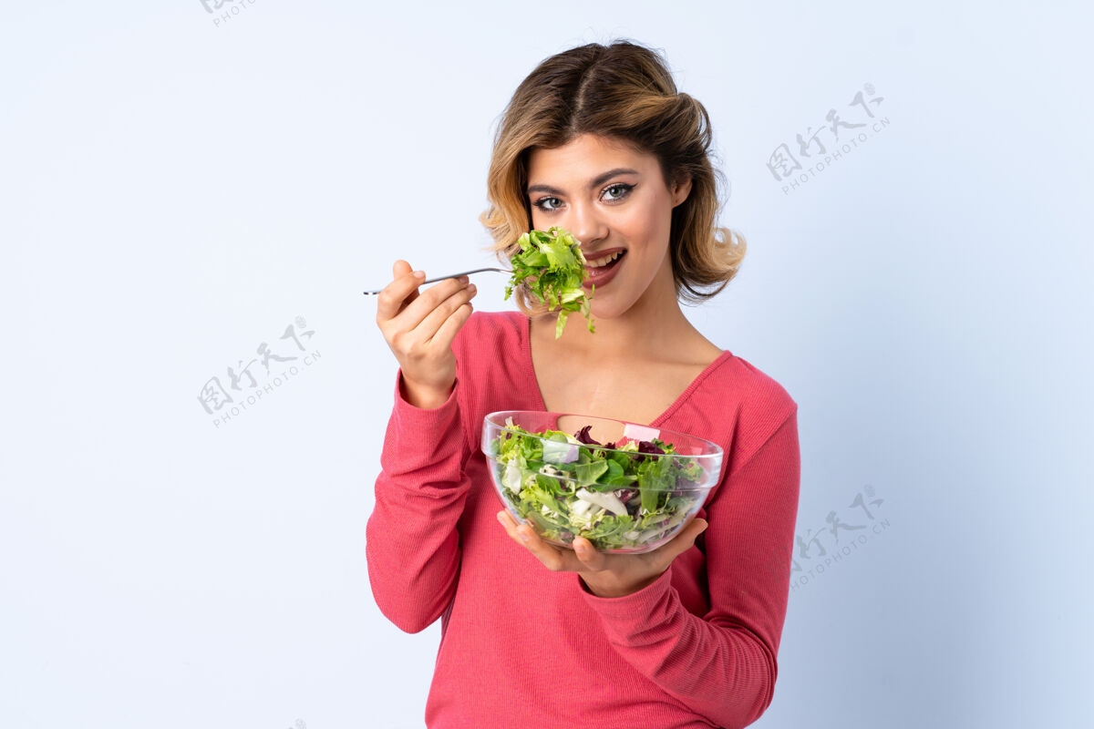 盘子一个十几岁的女人拿着色拉在蓝色上饮食人素食