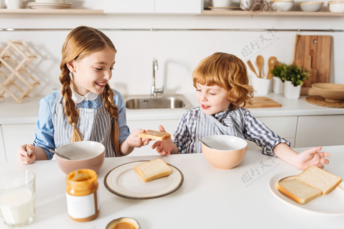 食物一个给你活泼一个可爱的女孩给她的弟弟一块花生酱面包 而他们两个早上都坐在桌子旁 一起享用早餐早餐玻璃千禧一代
