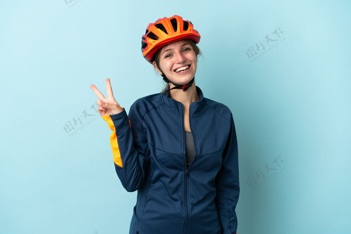 成年人在蓝色背景下 一位年轻的骑车女子面带微笑 展示着胜利的标志手女性是的
