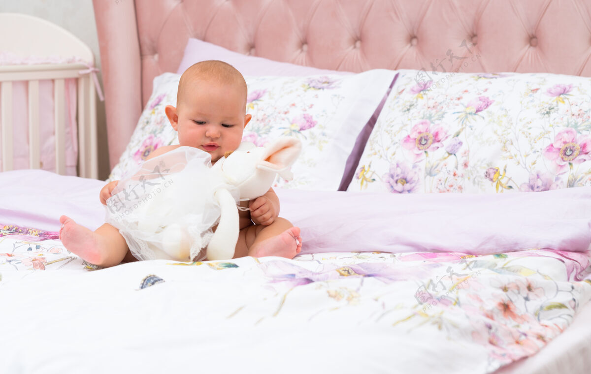 智力小女婴在有复印空间的托儿所的床上玩一个大毛绒玩具坐着天使毛绒绒