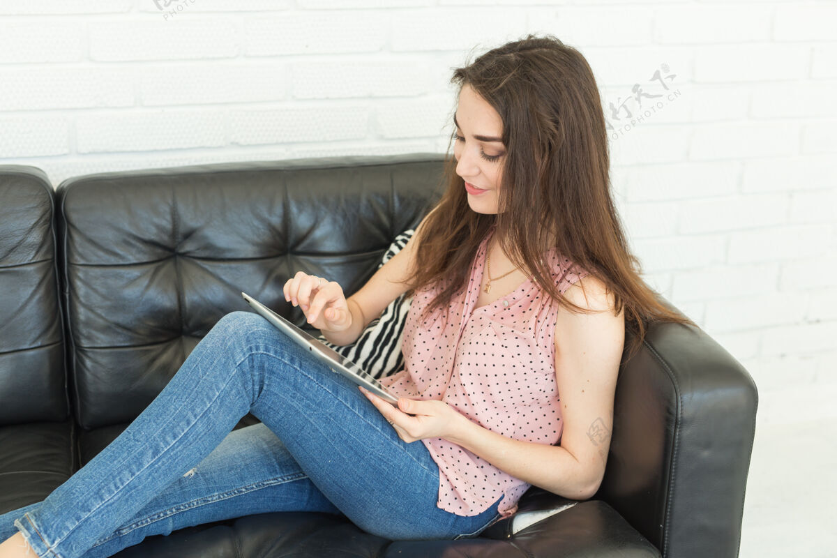 博客科技 通讯 人的概念——年轻女子坐在沙发上 坐在平板电脑里聊天 面带微笑设备使用白色