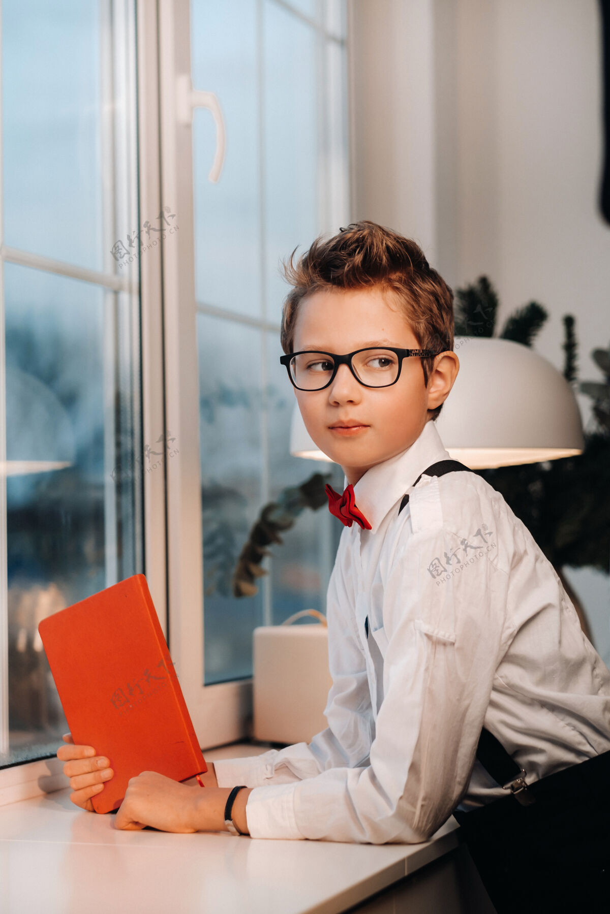 互动窗口站着一个男孩 穿着衬衫 打着红色领结 戴着眼镜 手里拿着一本红色的书举行领结青少年