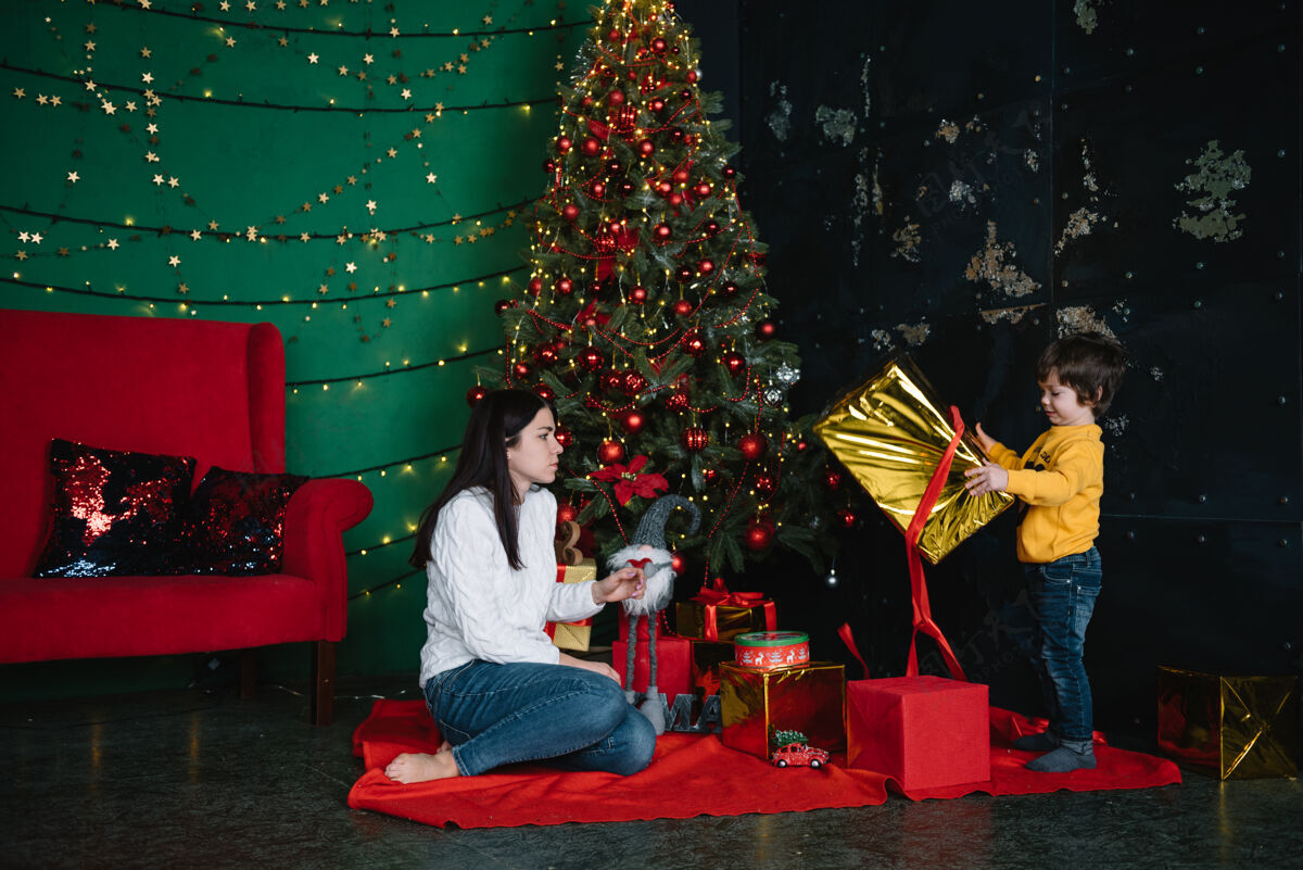 漂亮年轻美丽的母亲带着可爱的儿子在圣诞树旁礼物快乐圣诞节树成人家庭