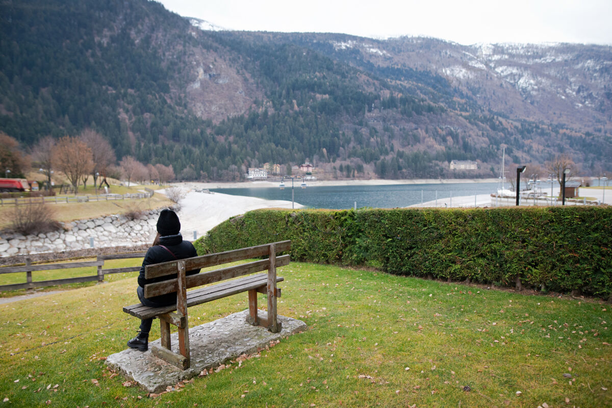 背光穿着暖和衣服的年轻女子独自坐在木凳上 在寒冷的日子里凝视着湖面长凳冠状病毒流行病