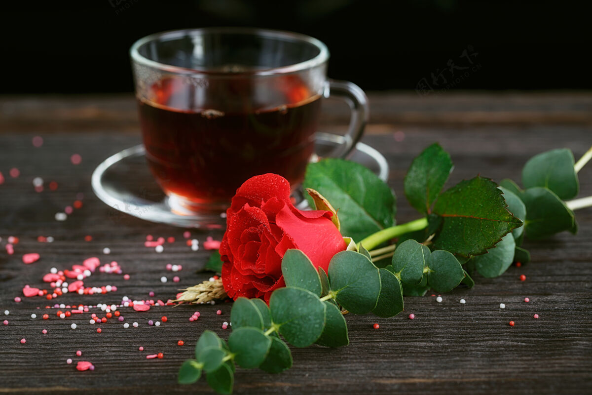 香气茶放在透明的杯子里 彩色的糖果和一朵红玫瑰放在暗处浪漫透明茶