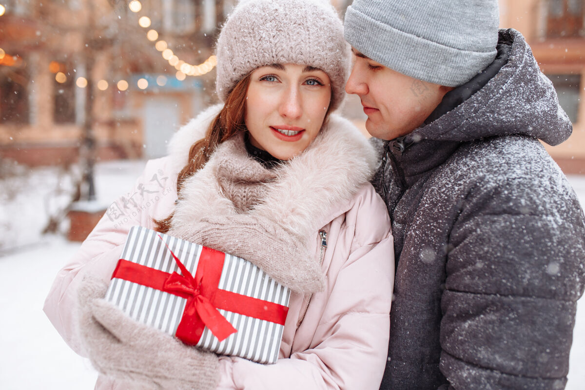 情侣一对幸福的情侣在冬天的雪景公园外 手里拿着红丝带的礼物手高兴男人和女人庆祝情人节一起日期在外面寒冷的冬日盒子欢呼女性