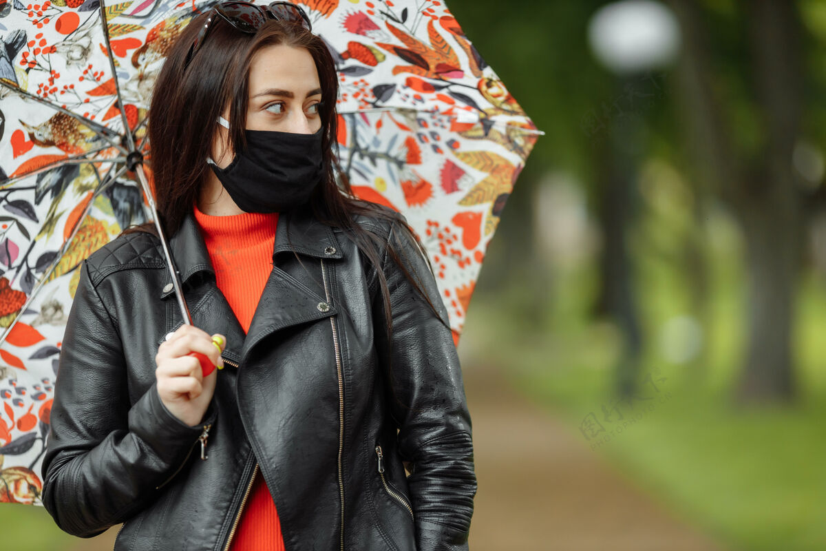 街道一个戴着面具的女孩走在街上一个戴着防护面具的女孩打着雨伞在公园里散步雨冠状病毒感染covid-19面罩长凳妇女