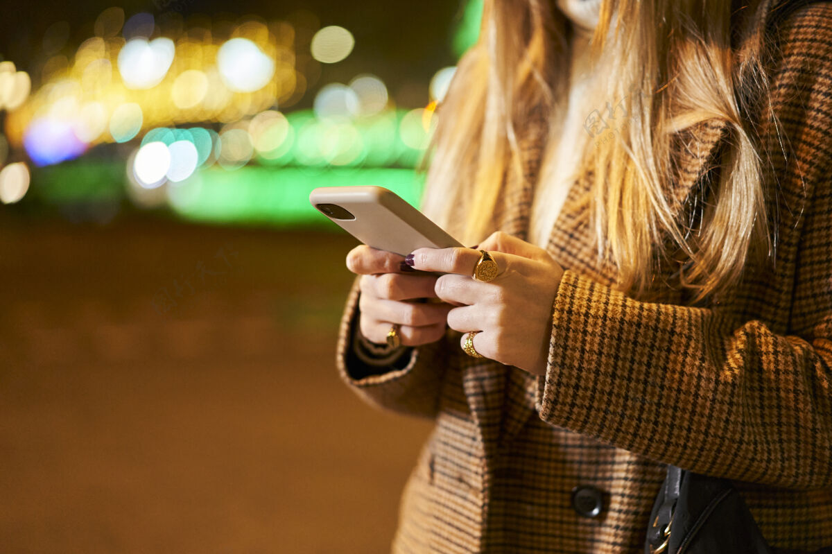 交通一个年轻的金发女人用智能手机写信息的特写镜头 在一个有背光和交通的城市里无法辨认人使用