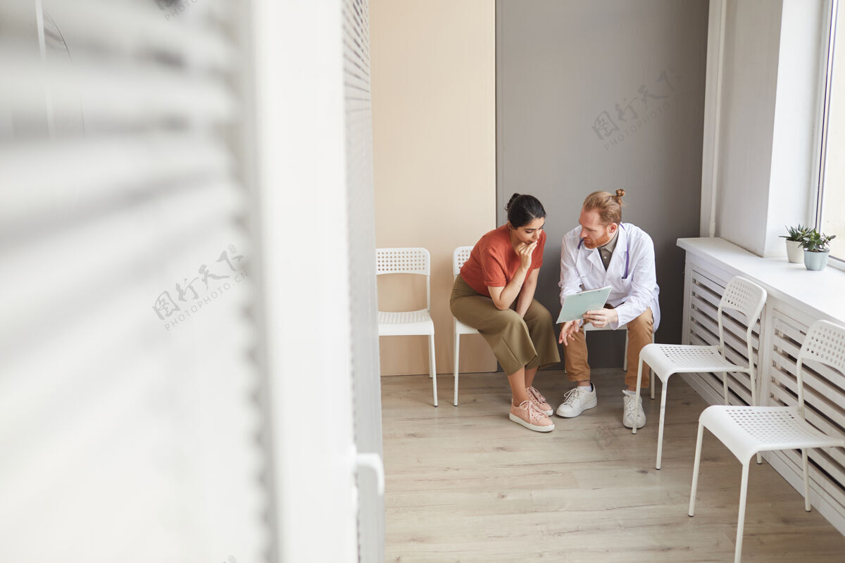 诊所男医生坐在走廊的椅子上给病人看结论医护人员人医疗职业