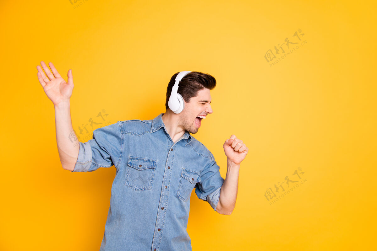 尖叫照片中疯狂的歌手对着想象中的麦克风尖叫着 用无线耳机隔着鲜艳的彩色墙壁听男人摇滚音乐家