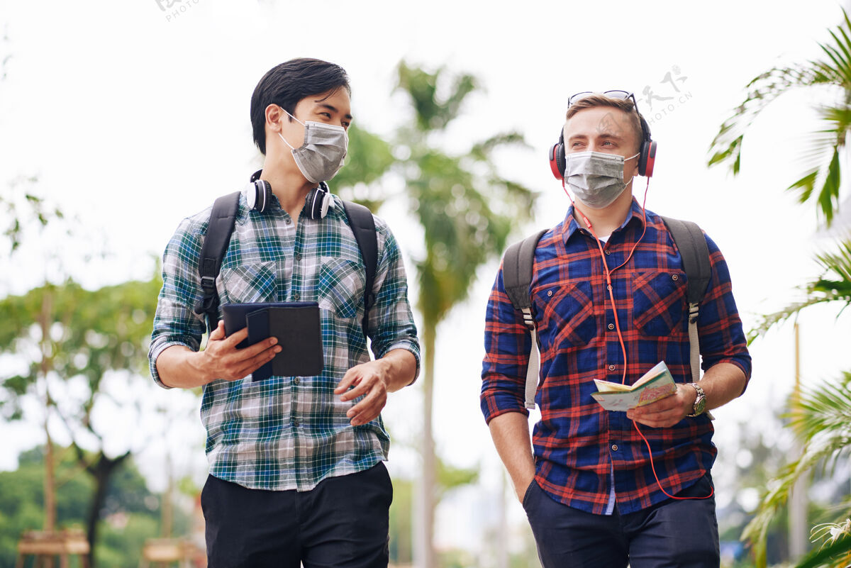 冠状病毒多民族年轻人背着背包走在街上 脸上挂着医学标志谈话讨论病毒
