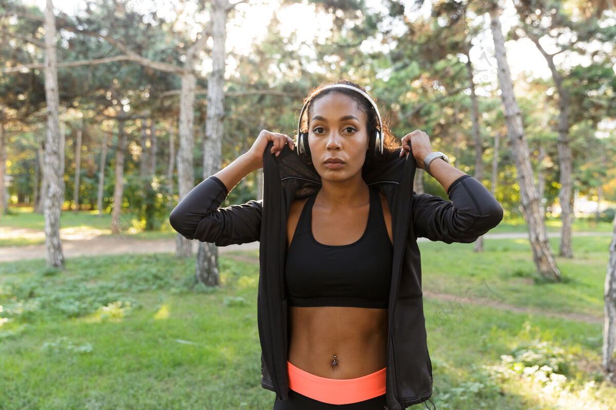 女性20多岁的女运动员穿着黑色运动服 戴着耳机 穿过绿色公园的肖像运动散步保健