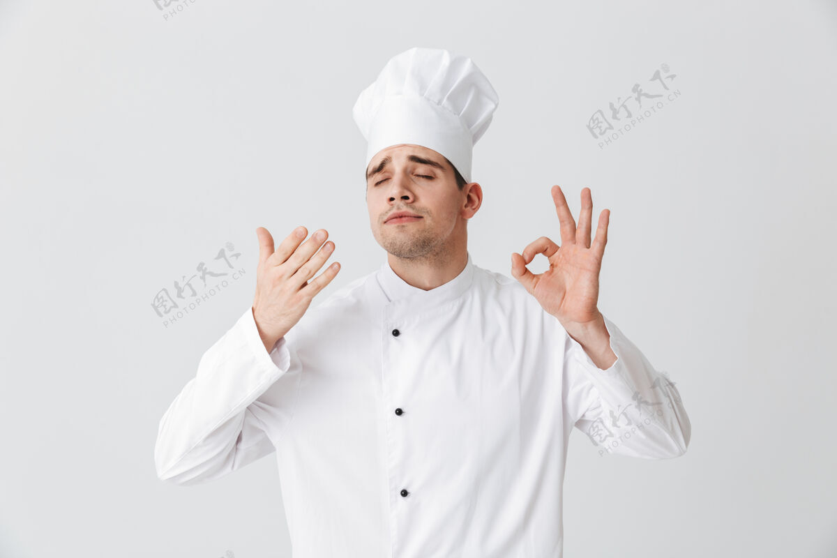 工作服开朗的厨师穿着制服品尝着隔着白墙的味道欢乐烹饪职业
