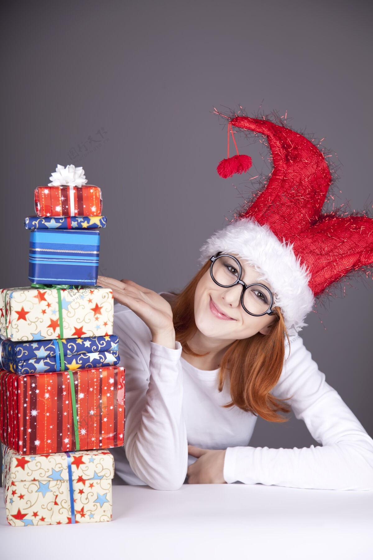 礼物滑稽的红发女孩戴着圣诞帽 戴着带礼盒的眼镜玩尼斯包装