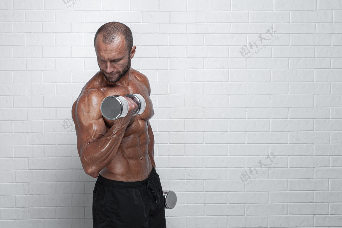 男人健美运动员在砖墙上用哑铃练习二头肌砖头成人健美