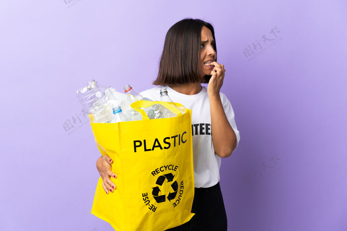 再利用年轻的拉丁女子拿着一个装满废纸的回收袋去回收孤立的紫色就有点紧张回收恐惧赛车