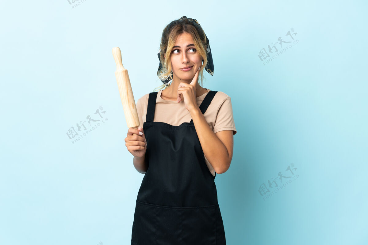 卷年轻的金发乌拉圭厨娘孤立在蓝色的怀疑和思考工作金发厨师