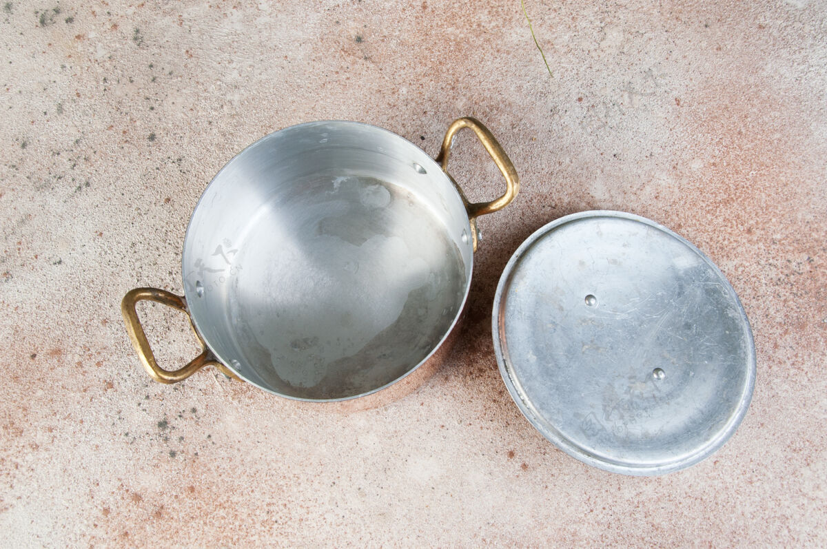 锅旧的铜砂锅 盖子和黄铜把手放在水泥桌上水平把手黄金