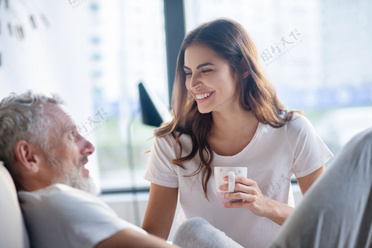 男人关闭我很高兴微笑倾听的女人坐在杯子旁 躺着严肃的男人在侧面婚礼发光在家