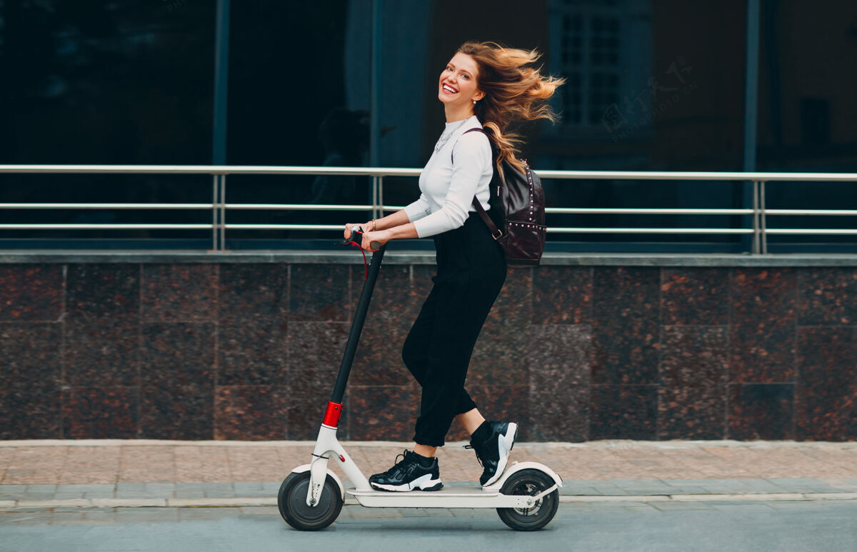 活动带着微笑的年轻女子在街上骑着电动滑板车积极城市女性