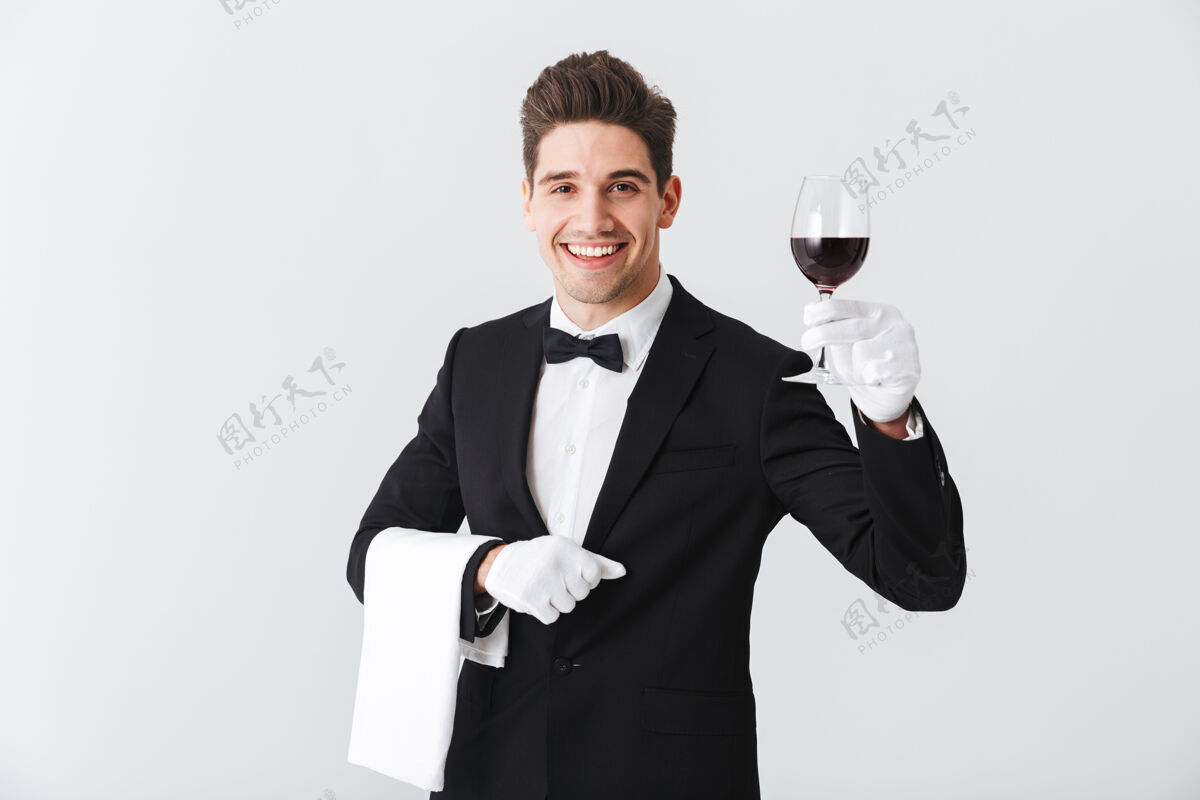 职业年轻帅气的侍者穿着燕尾服 端着一杯红酒隔着灰色的墙管家微笑火花
