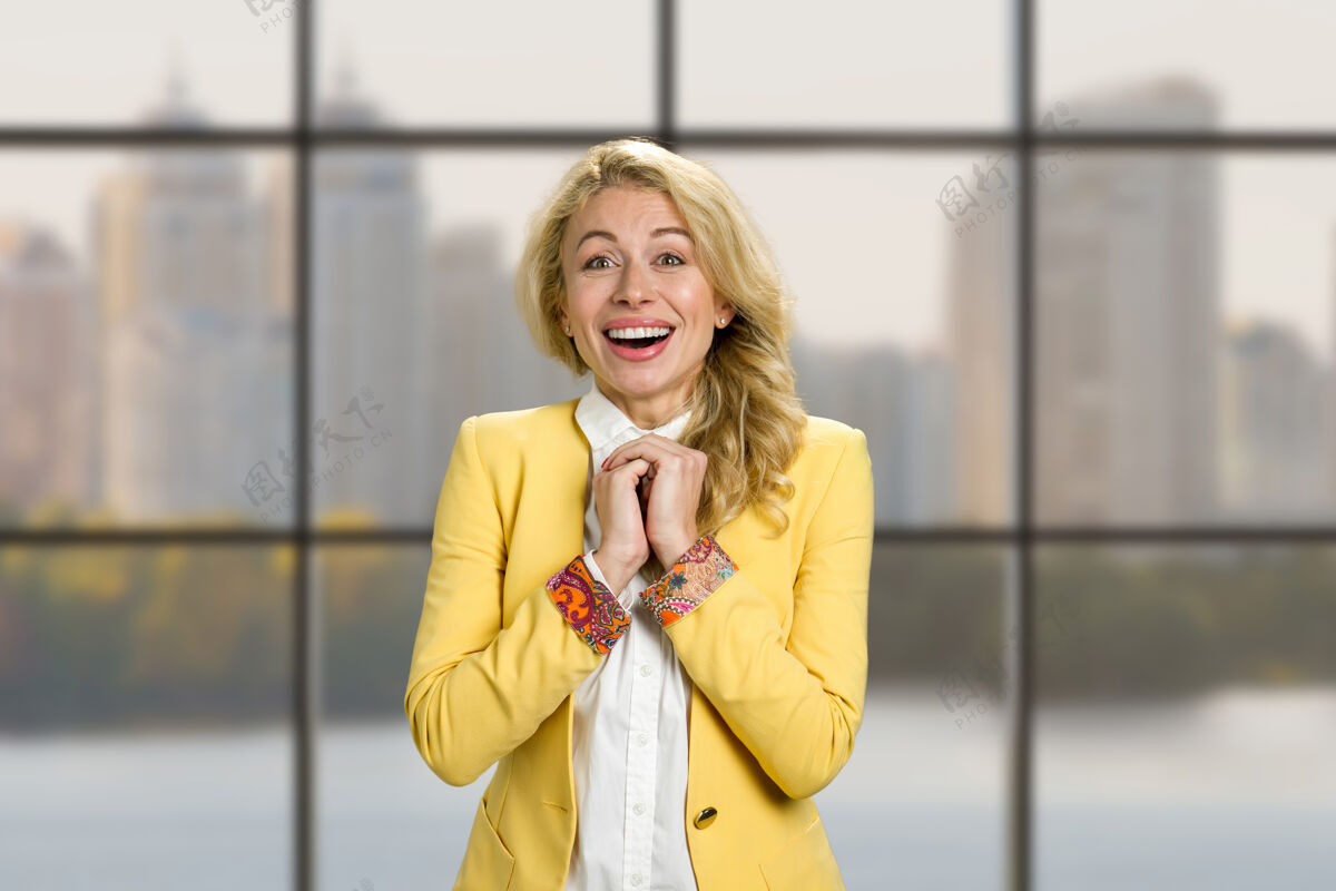 公司兴奋的快乐的商业女人的肖像兴奋的年轻快乐的女人握着紧握的手震惊地看着办公室的窗户控股喜悦金发