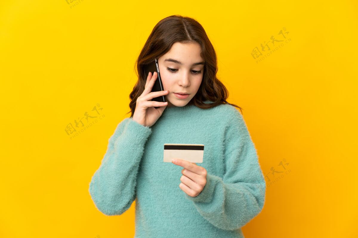 乐趣小白种女孩孤立的黄色背景购买手机与信用卡年轻孩子购物