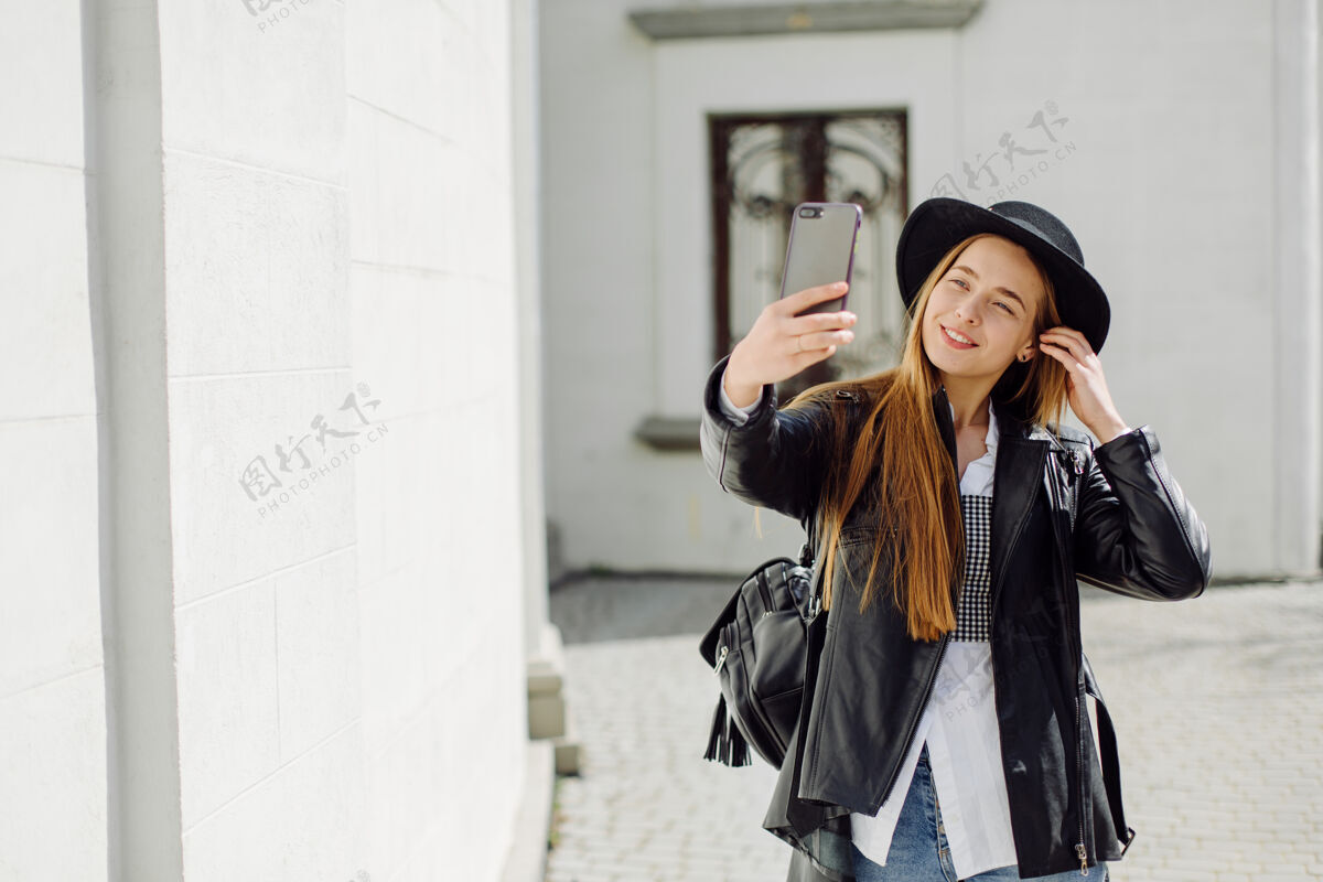 城市户外夏日写真的年轻时尚女孩在阳光明媚的日子摆在街上与手机混凝土移动应用程序