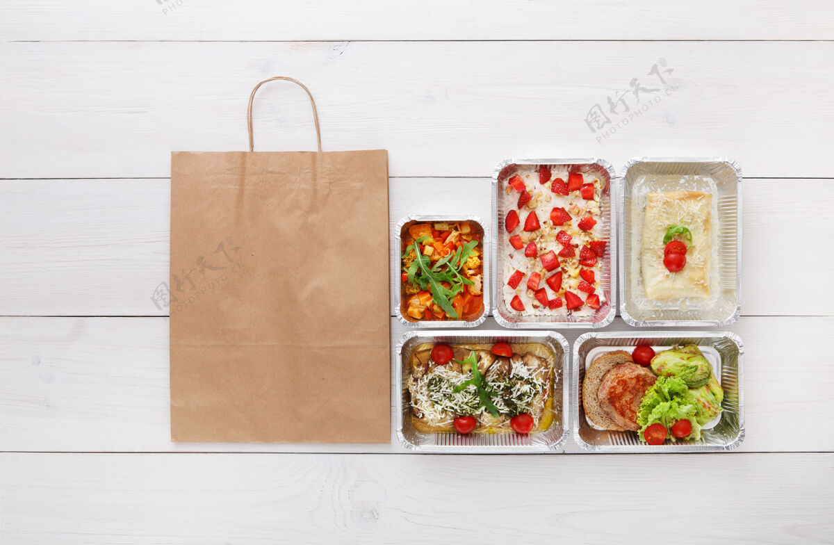 美食健康食品配送 日常膳食和零食营养 蔬菜 肉类和水果在铝箔盒和棕色纸袋包装俯视图 平放在白色木材与复制空间纸自然晚餐