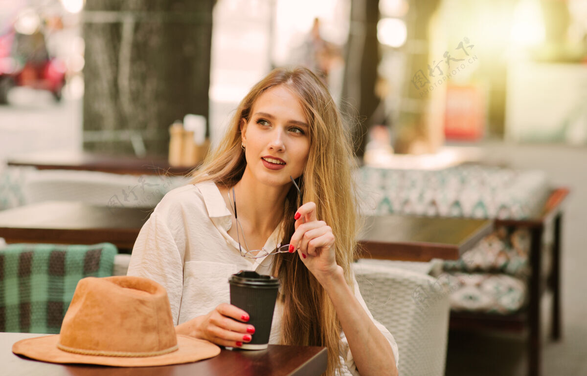 休闲快乐的金发女人坐在街上的咖啡馆里喝咖啡迷人的女人马克杯杯子