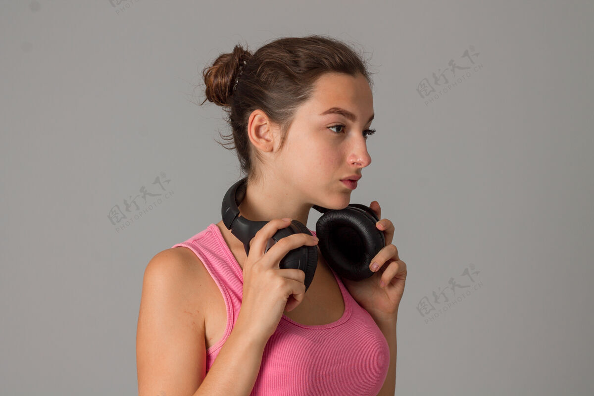 欢呼戴着耳机的年轻女子在灰色墙上的工作室里青少年时尚音乐
