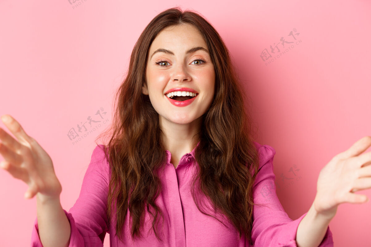 候选人特写照片中的快乐友好的女人微笑着 伸出双手欢迎或拥抱你 问候客人 站在粉红色的墙上请休闲积极