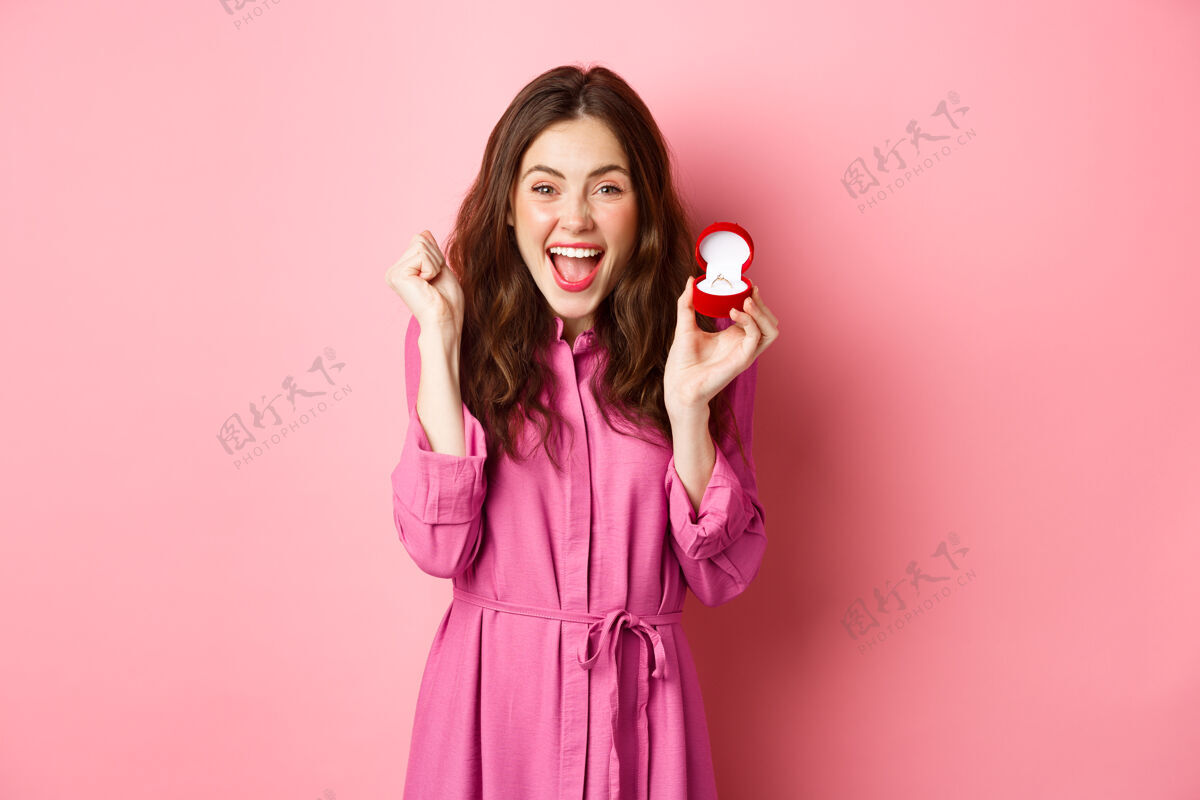 订婚兴奋的年轻女子展示订婚戒指和庆祝结婚 微笑快乐 谈论结婚的日子 接受求婚 站在粉红色的墙壁复制空间惊人微笑戒指
