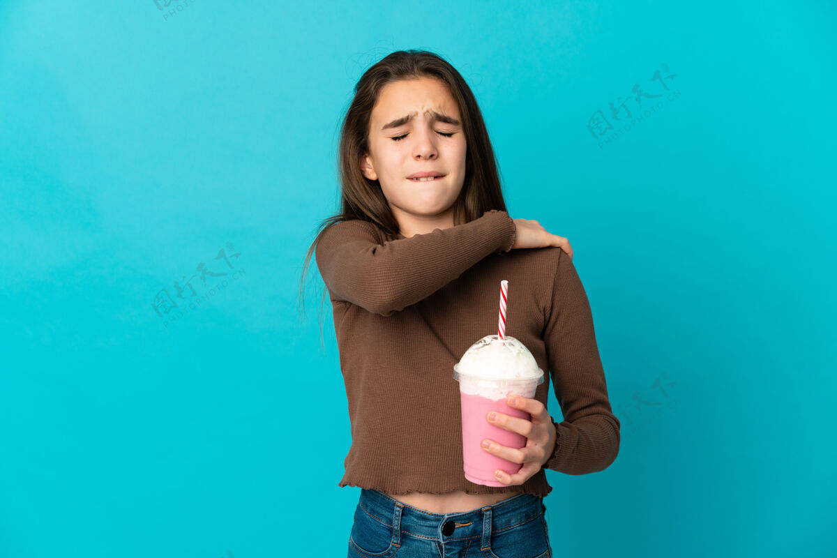 生病一个拿着草莓奶昔的小女孩被隔离在蓝色的墙上 因为努力而肩膀疼痛触摸身体可爱