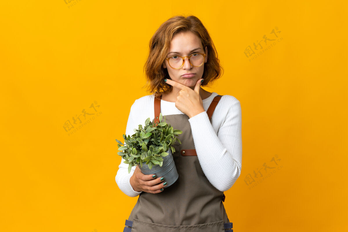 格鲁吉亚年轻的格鲁吉亚女人拿着一株隔离在黄色墙上的植物思考表达不知所措头发