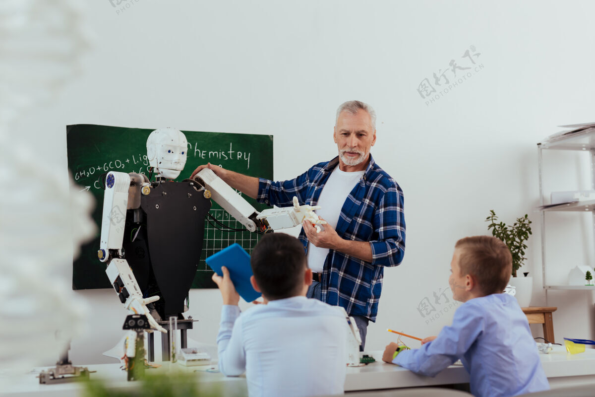 永远未来的科技积极的老人一边看着他的学生 一边告诉他们关于机器人的事情机械童年课程