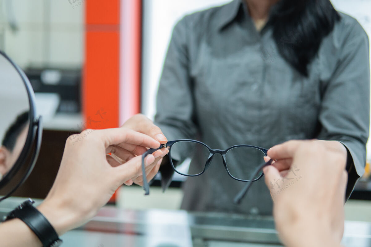 眼睛在一家眼镜店 售货员把一副眼镜递给顾客的手 这是选择性聚焦手消费者微笑
