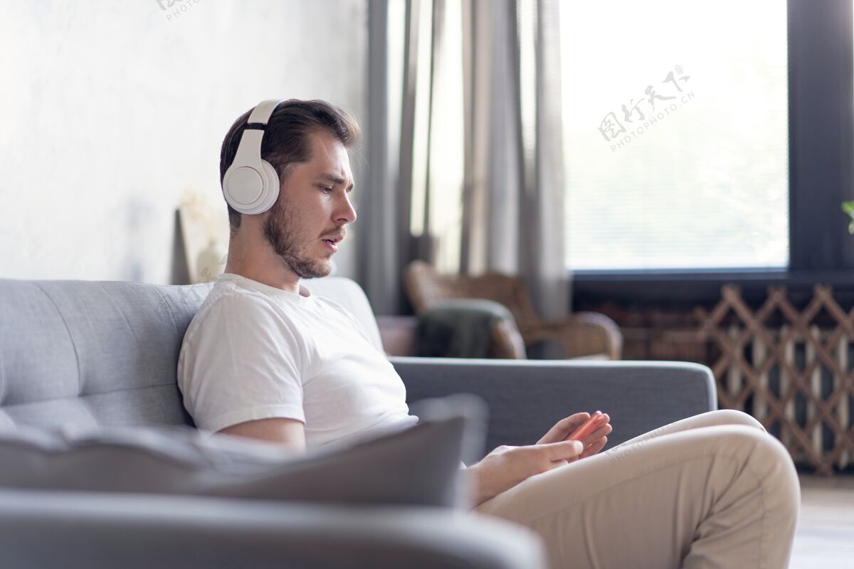 爱好快乐的年轻人戴着耳机 坐在家里的沙发上听音乐活动候选人技术
