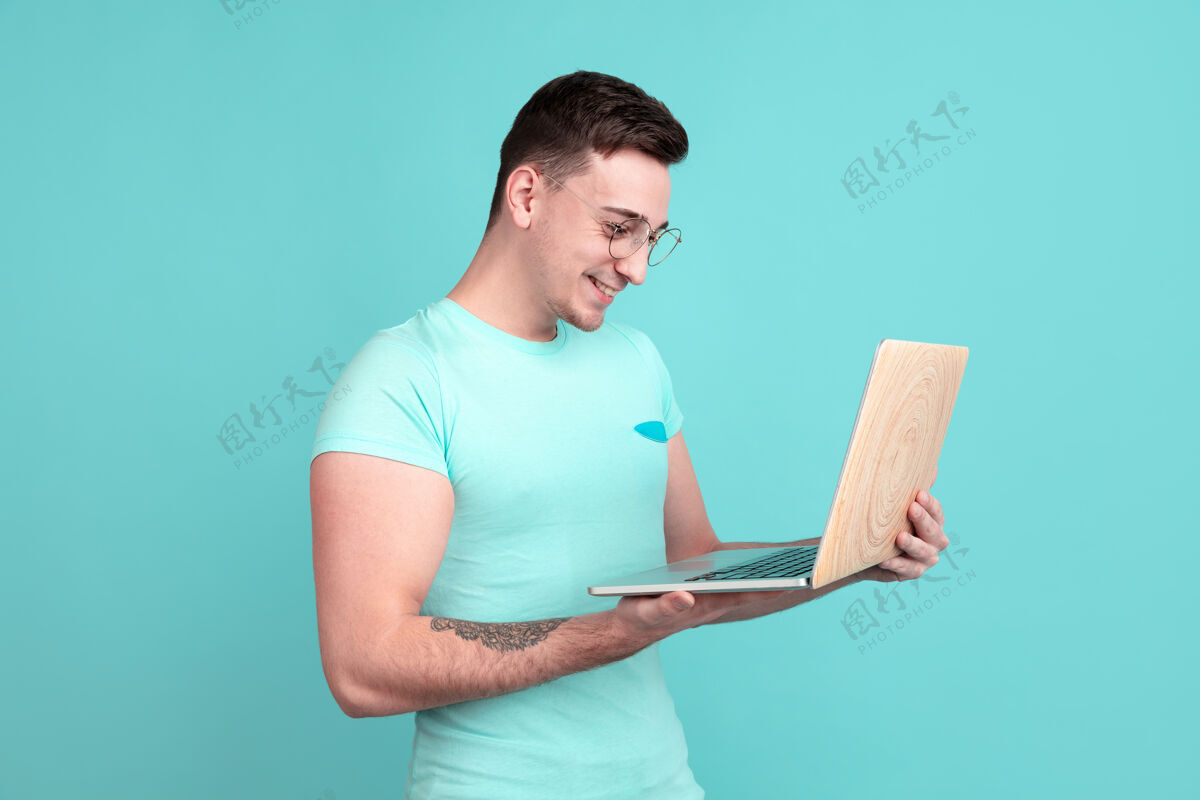 手势年轻人的肖像使用笔记本电脑隔离在海蓝宝石工作室墙上年轻人男性