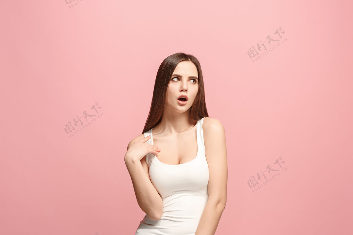 年轻沉思的女人 带着深思熟虑的表情 在粉红色的墙上做选择模特美丽沉思