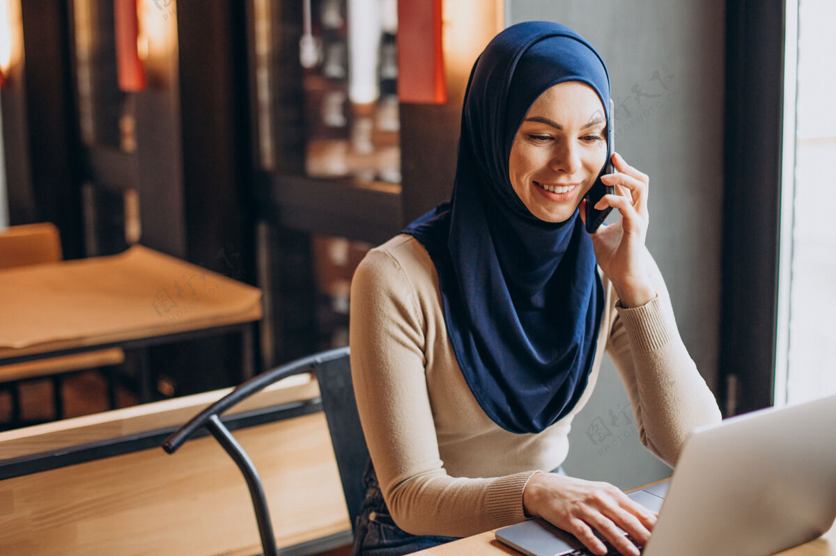 酒吧年轻的穆斯林妇女在咖啡馆里用电话和电脑文化学习成功