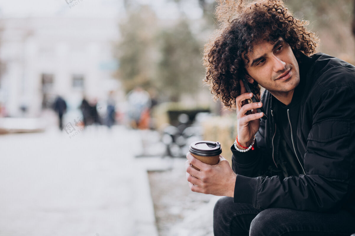 时髦卷发的年轻人一边喝咖啡一边打电话外卖黑发城市