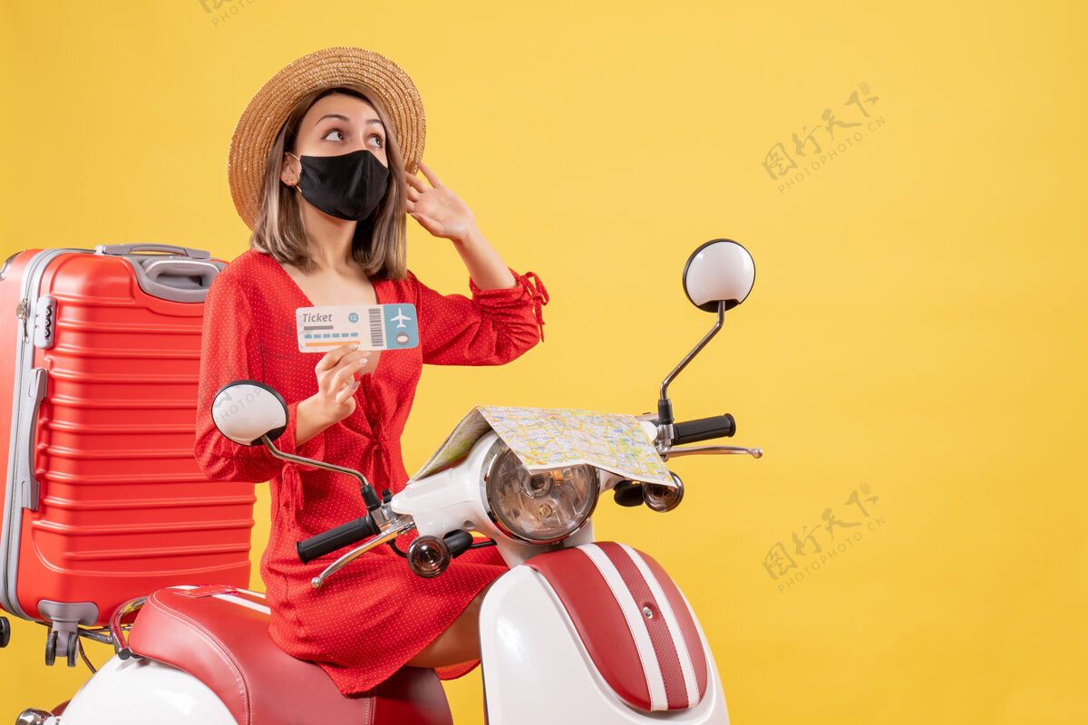 人正面图：戴着黑色面罩的年轻女士 骑着轻便摩托车 提着红色手提箱 拿着车票 在看什么东西冒险滑板车面具