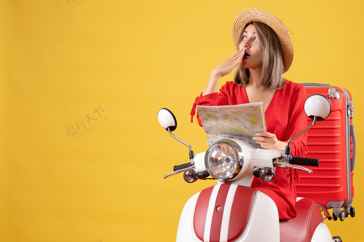肖像前视图：骑着轻便摩托车的年轻女士拿着红色手提箱拿着地图在想什么轻便摩托车红色旅游